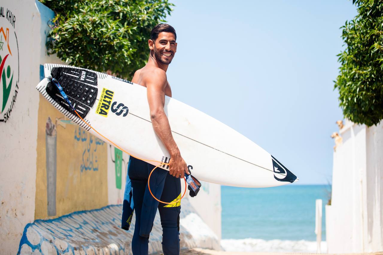 Hamza El Bahraoui smiling with surfboard near the ocean in Taghazout